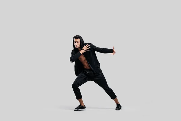 Bonito jovem dançarino de rua dançando vestido com calças pretas, uma camisola em um tronco nu e um capuz dança em um fundo branco — Fotografia de Stock