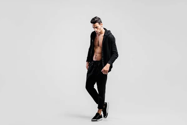 Jeune beau danseur vêtu d'un pantalon noir et d'un sweat-shirt sur un torse nu se tient sur le fond blanc — Photo