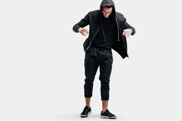 Dark-haired stylish dancer wearing black clothes and a hood makes stylized movements of street dance. — Stock Photo, Image