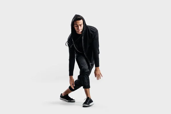 Dark-haired stylish dancer wearing black clothes and a hood makes stylized movements of street dance. — Stock Photo, Image