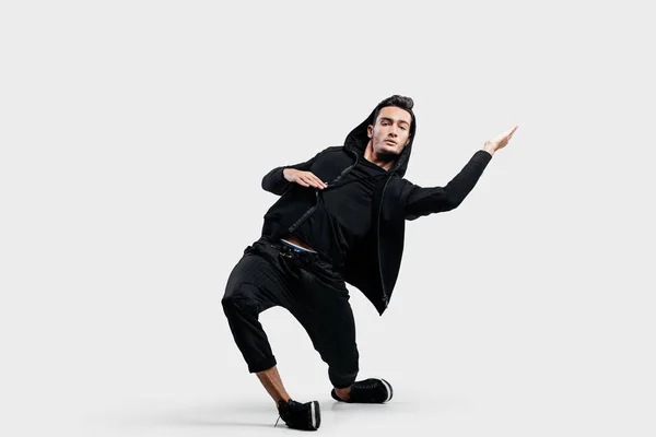 Mörkhårig snygg dansare bär svarta kläder och en huva gör stiliserade rörelser av streetdance. — Stockfoto