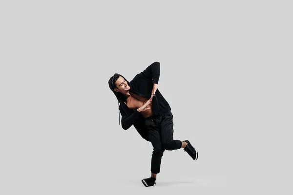 Jovem dançarina bonita vestida de calças pretas, uma camisola em um tronco nu está dançando dança de rua. Ele faz movimentos estilizados com as mãos — Fotografia de Stock