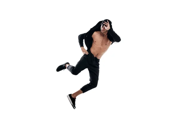 Jovem bonito jovem dançarino de rua dançando vestido com calças pretas, uma camisola em um tronco nu pula sobre um fundo branco — Fotografia de Stock