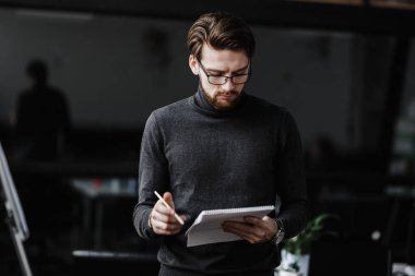 Rahat ofis tarzı giysiler giymiş adam modern ofiste bir defter notları yapar