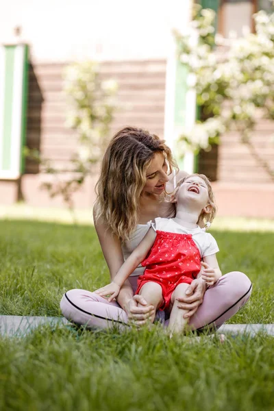 Genç anne ve küçük kızı sıcak bir yaz gününde bahçede çim oturan eğlenin — Stok fotoğraf