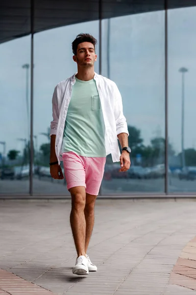 Élégant gars habillé en vêtements d'été à la mode dans un style décontracté posant sur le fond d'un bâtiment en verre un jour d'été — Photo