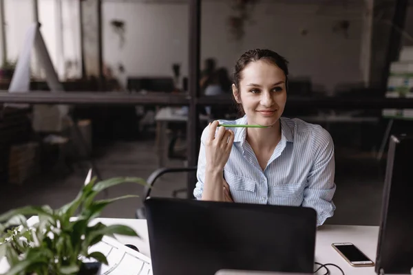 Young woman dressed in office style clothes is working at the laptop sitting at desk in the light modern office