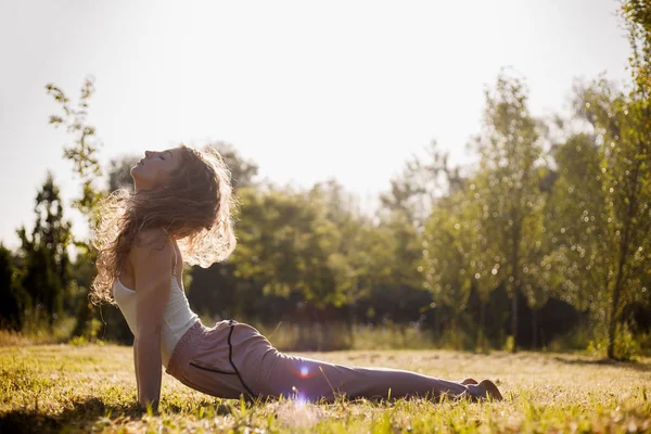 Junge Frau in Yoga-Kleidung praktiziert Yoga an der frischen Luft in der Natur auf dem Rasen an einem sonnigen Tag — Stockfoto