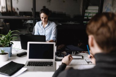 Genç kadın ve adam ofis tarzı giysiler giymiş modern ofis ekipmanları ile donatılmış ışık modern ofiste masalarında oturan çalışıyoruz