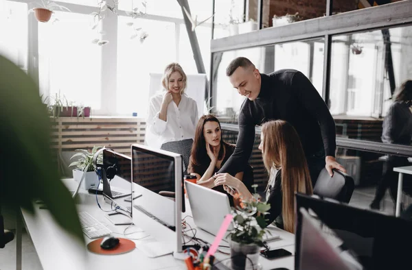 Et ungt team jobber på et skrivebord med datamaskin og bærbare datamaskiner i et moderne, åpent romkontor. – stockfoto