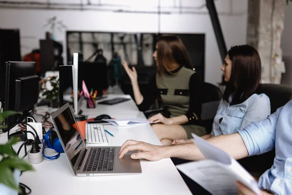 Et ungt team av kolleger jobber på pulten med en bærbar datamaskin og dokumenter i et lett, moderne kontor – stockfoto