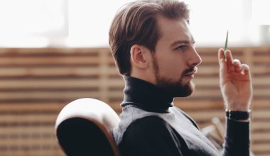 Rahat ofis tarzı giysiler giymiş adam modern ofiste elinde kalem ile bir ofis sandalyesinde oturuyor