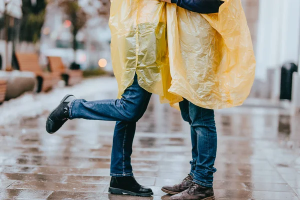 Ноги парня и девушки в джинсах и желтых плащах на улице под дождем — стоковое фото