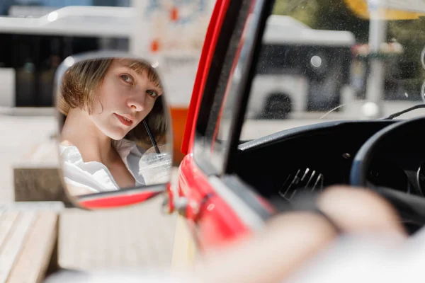 O reflexo no espelho minivans da jovem mulher em um chapéu de palha vestido com camisa branca bebendo um milkshake em um dia ensolarado de verão — Fotografia de Stock