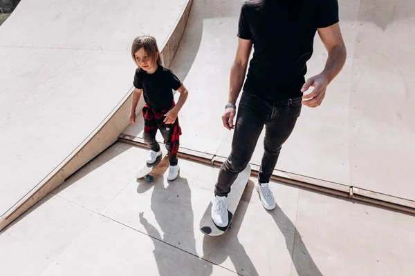 Glücklicher Vater und sein kleiner Sohn in legerer Kleidung fahren Skateboards in einem Skatepark mit Rutschen am sonnigen Tag — Stockfoto