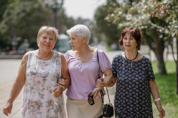 Three old women walking together in the park on a warm day