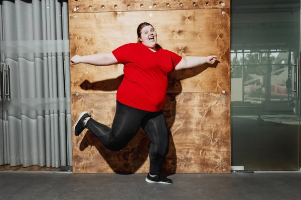 체육관에서 나무 벽의 배경에 스포츠웨어 점프에서 옷을 입고 재미 뚱뚱한 소녀 — 스톡 사진