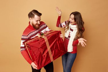 Kız surprisly büyük bir hediye tutan adam bakar. Her ikisi de kırmızı ve beyaz kazak lar içinde geyikli.