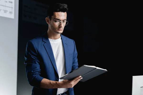 Junger gutaussehender Architekt mit Brille im blau karierten Sakko macht sich im Büro Notizen in einem Notizbuch Stockfoto