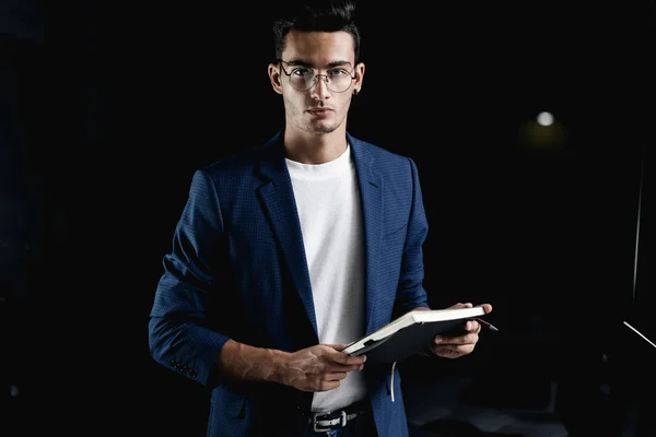 Élégant jeune architecte en lunettes vêtu d'une veste à carreaux bleu garde un carnet dans ses mains dans le bureau Photo De Stock