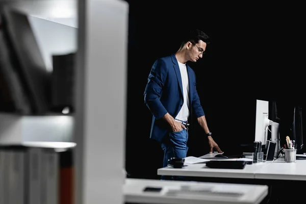 Architecte professionnel élégant en lunettes vêtu d'une veste à carreaux bleus se tient à côté du bureau avec ordinateur dans le bureau Images De Stock Libres De Droits