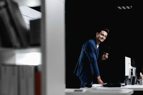 Stilvoller professioneller Architekt mit Brille im blau karierten Sakko steht neben dem Schreibtisch mit Computer im Büro lizenzfreie Stockbilder