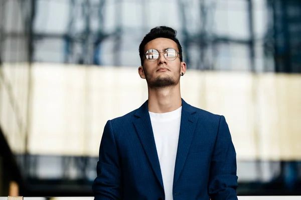 Architecte en lunettes habillé de vêtements élégants se dresse sur le fond d'un bâtiment en verre moderne — Photo