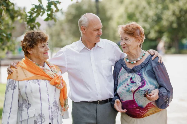 Ein alter Mann und zwei alte Frauen spazieren an einem warmen Tag fröhlich zusammen in einem Park Stockbild