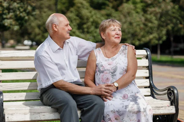 Gammel mann og gammel dame sitter sammen på benken i en park på en varm dag stockbilde