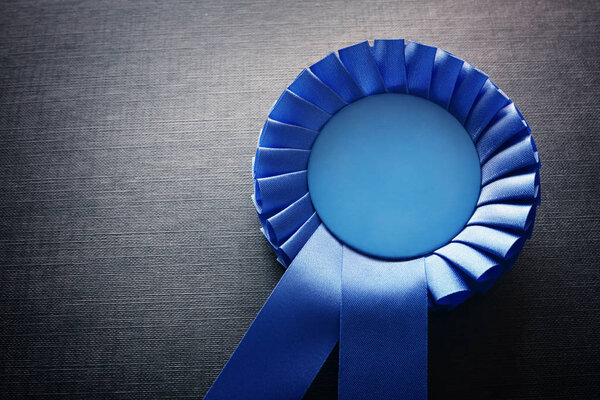 Blue award rosette with ribbons and copy space on black background