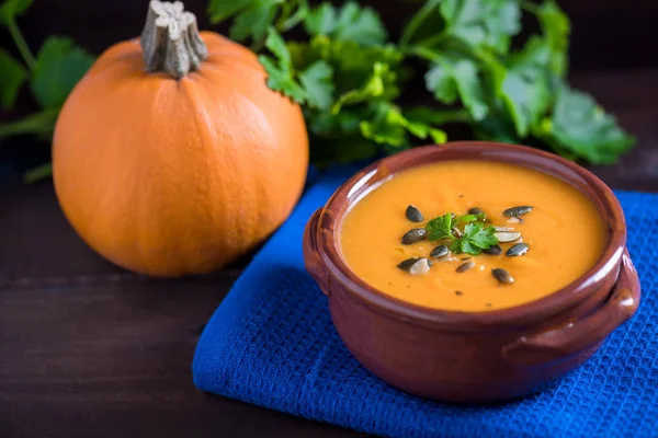 Gros plan de soupe de citrouille brillante dans un bol avec du persil, de l'huile d'olive et des graines de citrouille sur un fond en bois foncé . — Photo