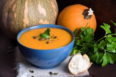 Bir kase kabak çorbası, maydanoz, zeytinyağı ve kabak çekirdeği ile servis. Vegan çorba. Koyu ahşap arka plan.