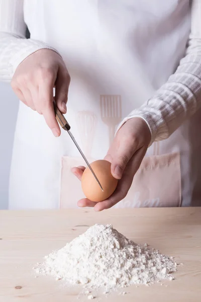 Young woman breaks egg above white flour to make dough for pasta — Stock Photo, Image