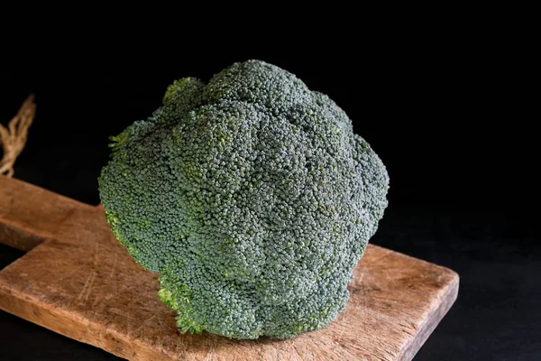 Fresh broccoli on a cutting board on a black background, rustic style, dark key. Healthy food — Stock Photo, Image