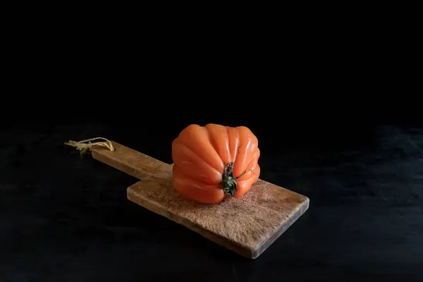 Pomodoro brutto succoso colorato su tagliere di legno su un backgound nero, stile rustico e basso tasto — Foto Stock