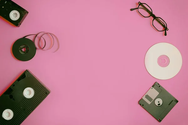 Dispositivos de almacenamiento retro: placa, dos videocasetes, disquete, CD y vasos. Concepto de tecnología obsoleta sobre fondo de papel rosa, vista superior, minimalismo —  Fotos de Stock