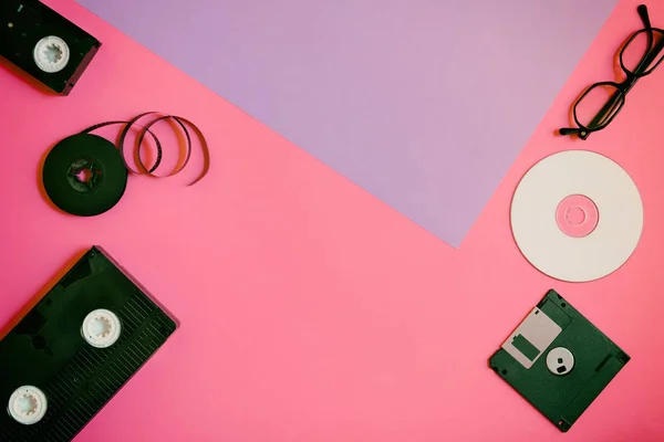 Retro lagerenheder: plade, to videokassette, diskette, CD og briller. Forældet teknologi koncept på lyserød og violet papir baggrund, top view, minimalisme - Stock-foto