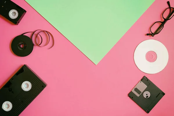 Dispositivi di memorizzazione retrò: piastra, due videocassette, floppy disk, CD e occhiali. Concetto di tecnologia obsoleto su sfondo di carta rosa e menta, vista dall'alto, minimalismo — Foto Stock