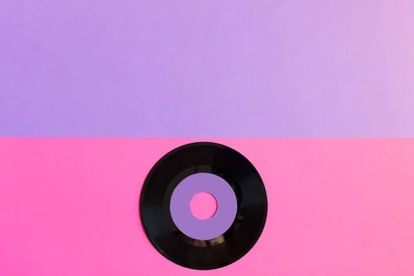 Un disco de vinilo anticuado sobre un fondo de papel de dos toneladas: rosa y violeta, cultura pop. Vista superior. Minimalismo, vista superior con espacio de copia — Foto de Stock