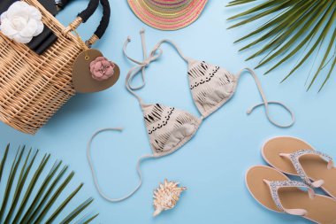 Palmiye yaprakları ile yaz arka plan, moda şapka, Bikini, Flip flop, Açık pastel mavi arka plan üzerinde saman plaj çantası, seyahat ve tatiller kavramı, üst görünüm