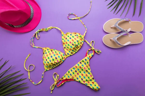 Summer background with palm leaves, pink fashion hat and bikini on violet or purple background, travel and vacations concept, top view