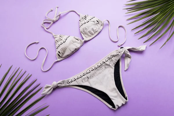 Fondo de verano con hojas de palma y bikini sobre fondo violeta o púrpura, viaje y concepto de vacaciones, vista superior — Foto de Stock