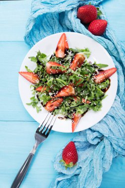 Arugula ile sağlıklı organik diyet salatası, çilek ve susam beyaz plateon içinde Balsamik sır ile pastel mavi ahşap arka plan, üst görünüm