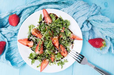 Arugula ile sağlıklı organik diyet salatası, çilek ve susam beyaz plateon içinde Balsamik sır ile pastel mavi ahşap arka plan, üst görünüm
