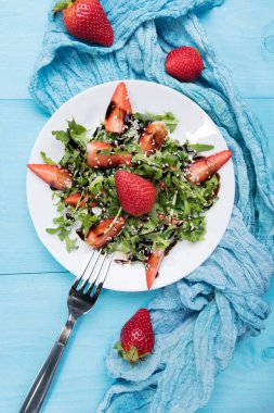 Arugula ile sağlıklı organik diyet salatası, çilek ve susam beyaz plateon içinde Balsamik sır ile pastel mavi ahşap arka plan, üst görünüm