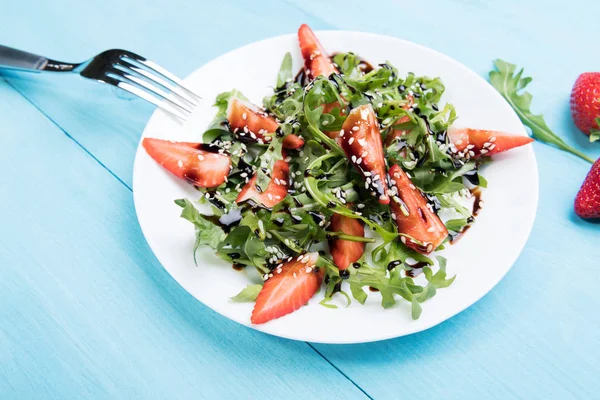 Ensalada saludable dieta orgánica con rúcula, fresas y sésamo con esmalte balsámico en meseta blanca un fondo de madera azul pastel, vista superior — Foto de Stock