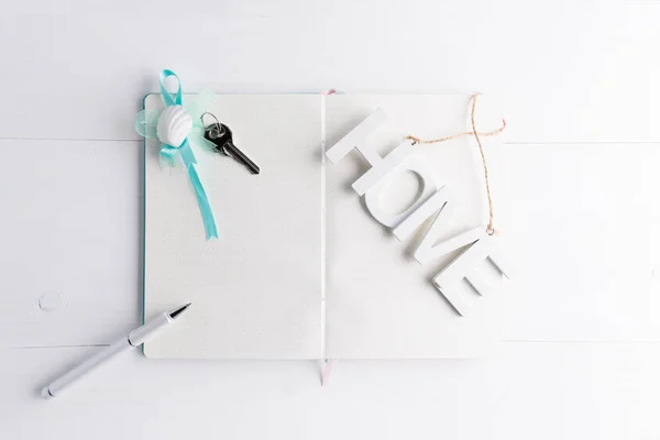 White blank page of notebook and pen on the left hand side, home key on a white wooden background with copy space, mortgage, debt or property loan