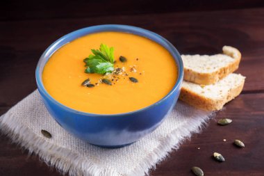 Bir kase kabak çorbası, maydanoz, zeytinyağı ve kabak çekirdeği ile servis. Vegan çorba. Koyu ahşap arka plan.