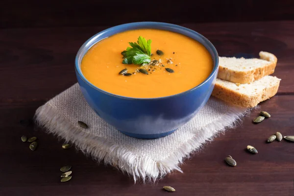 Bir kase kabak çorbası, maydanoz, zeytinyağı ve kabak çekirdeği ile servis. Vegan çorba. Koyu ahşap arka plan.