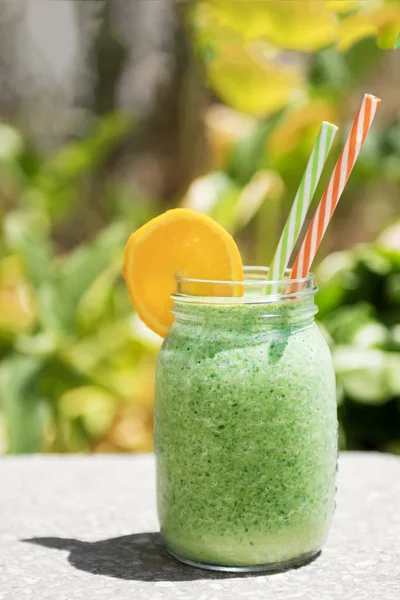 Summer healthy detox drink: blended green smoothie in a city park or garden in the bright midday sun